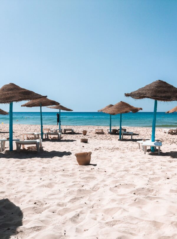 Peaceful sandy beach with straw umbrellas and clear blue sea under a bright sky.