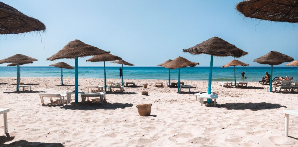 Peaceful sandy beach with straw umbrellas and clear blue sea under a bright sky.