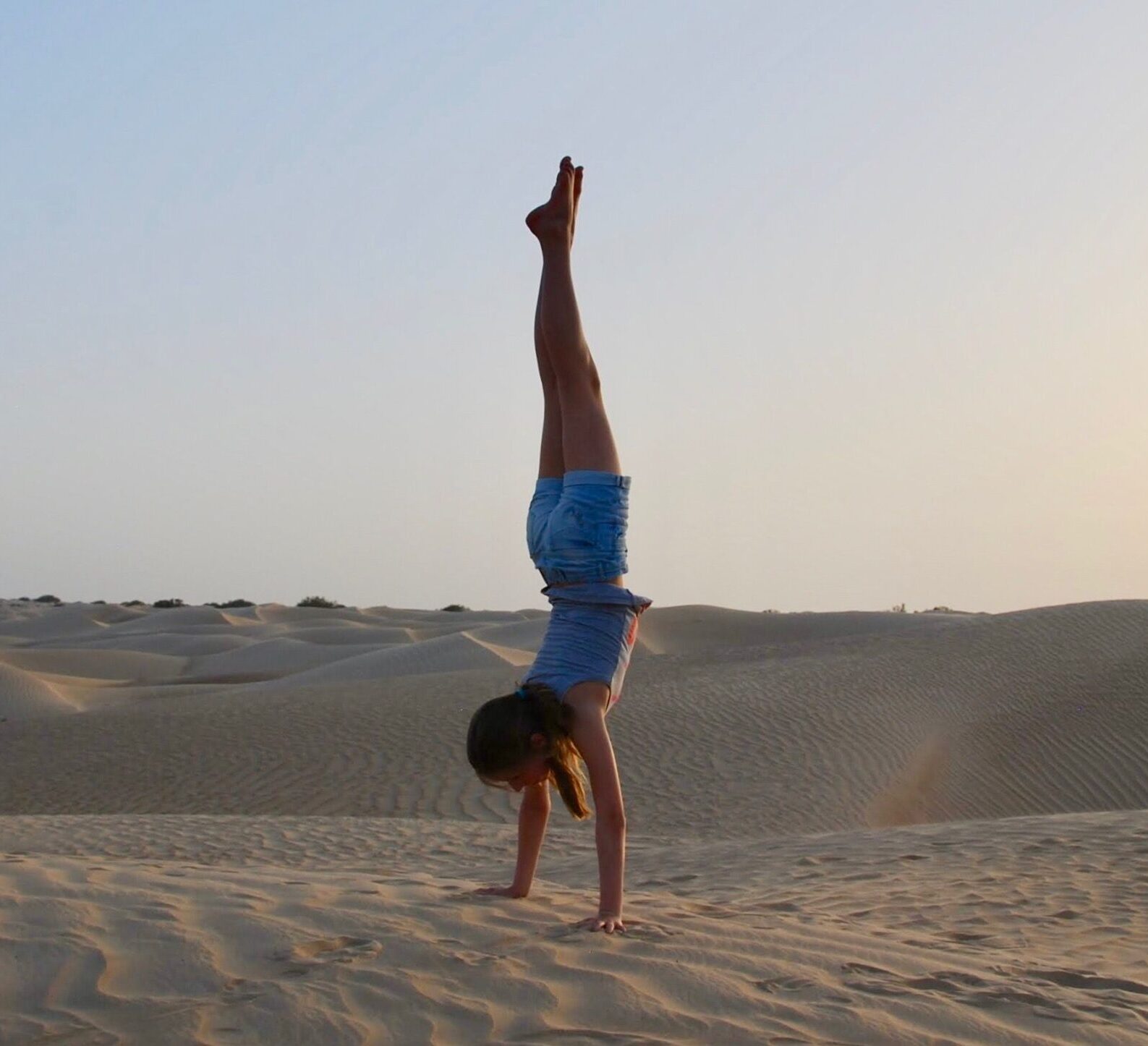 A woman performs a handstand on sand dunes at sunset in the Omani desert, showcasing balance and tranquility.