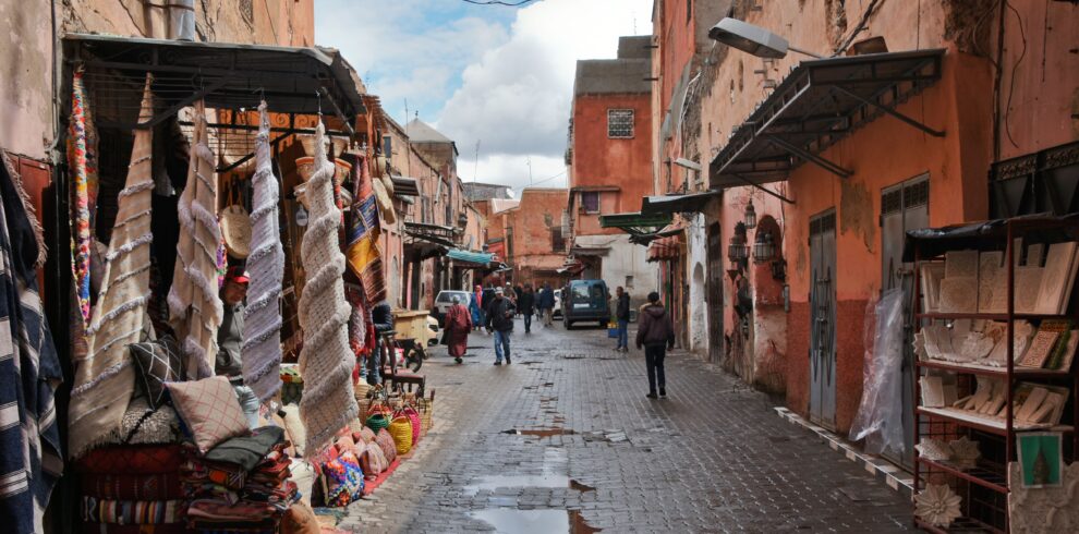 Explore the bustling streets of Marrakech with vibrant fabrics and traditional architecture in this lively market scene.