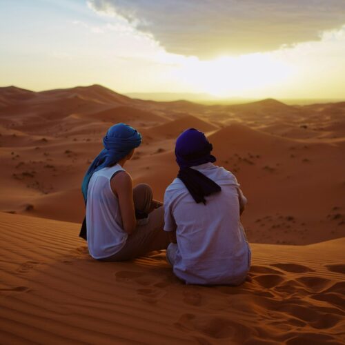 Two travellers sitting on top of Erg Chebbi sand dunes at sunset