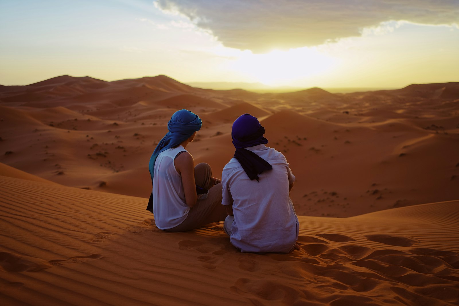 Two travellers sitting on top of Erg Chebbi sand dunes at sunset