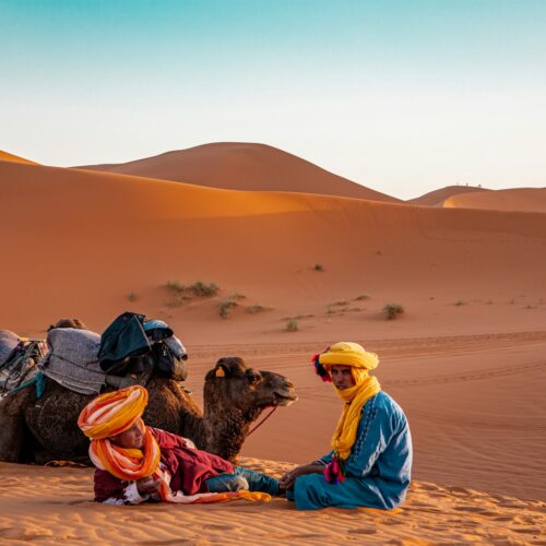 Man in traditional robe sitting on sand dunes near Merzouga, Morocco