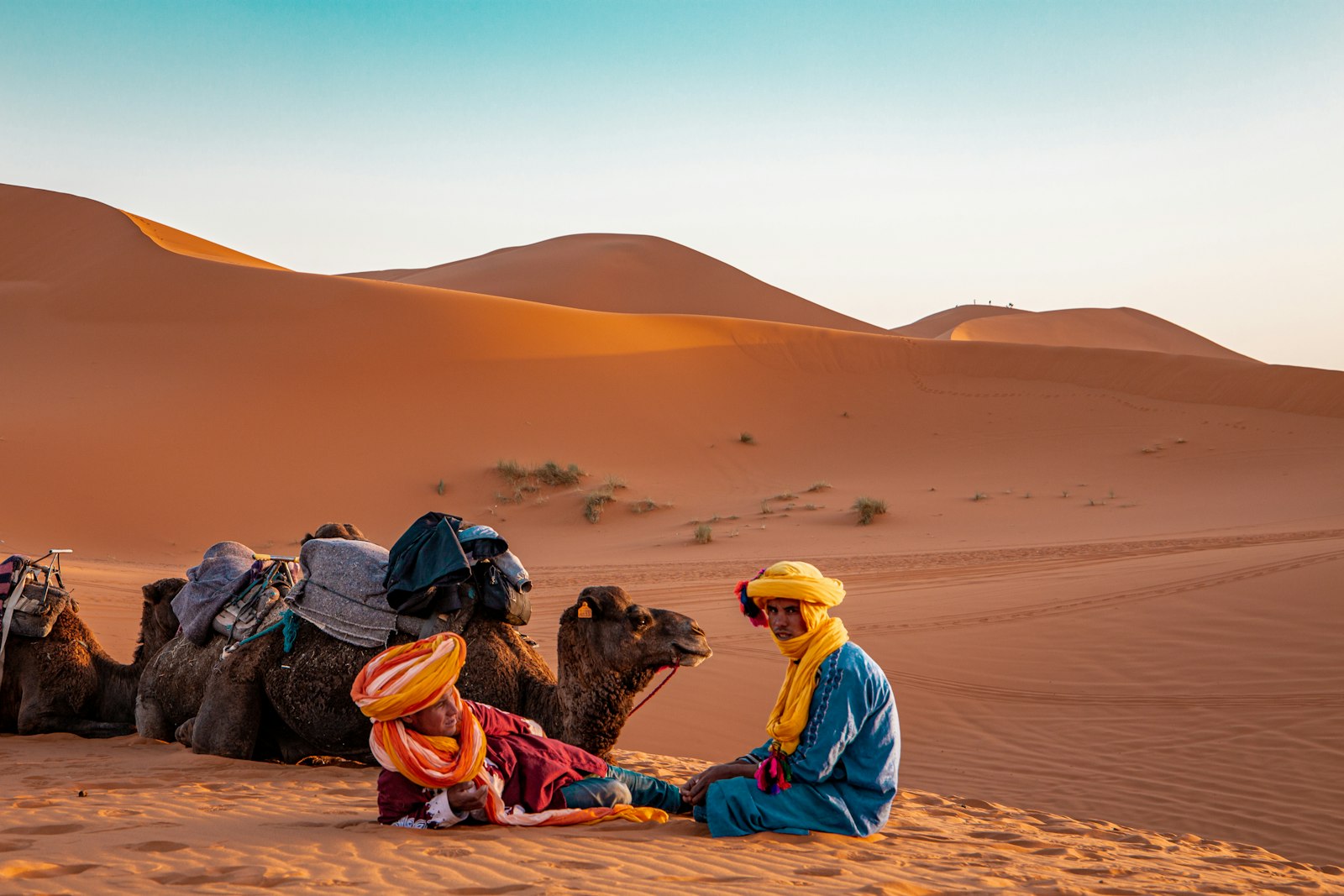 Man in traditional robe sitting on sand dunes near Merzouga, Morocco